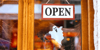 An OPEN sign and white ghost hanging in a storefront door window