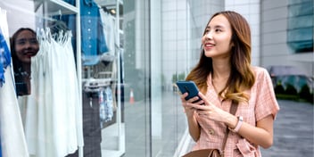 A woman looking up from her phone into a retail store, meant to represent the power of retail media trends in 2026.