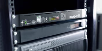 A close up of the new Rockbot Smart Amp in an AV rack, showing the back side of the device to highlight how easy it is to get started. The following features are visible in the image: Audio In, Status, Volume, and Speaker Output.