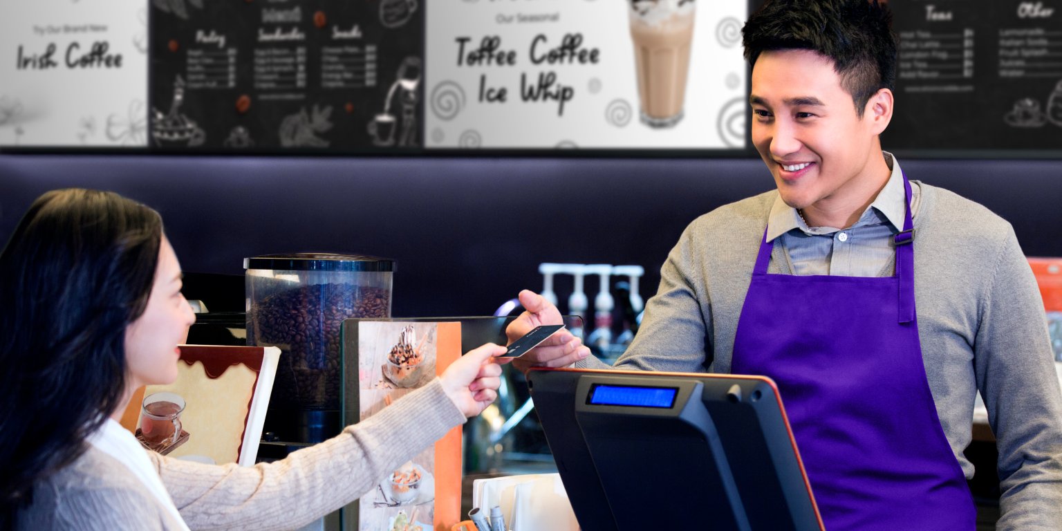 Barista at counter with menu boards behind him showing the benefits of digital signage
