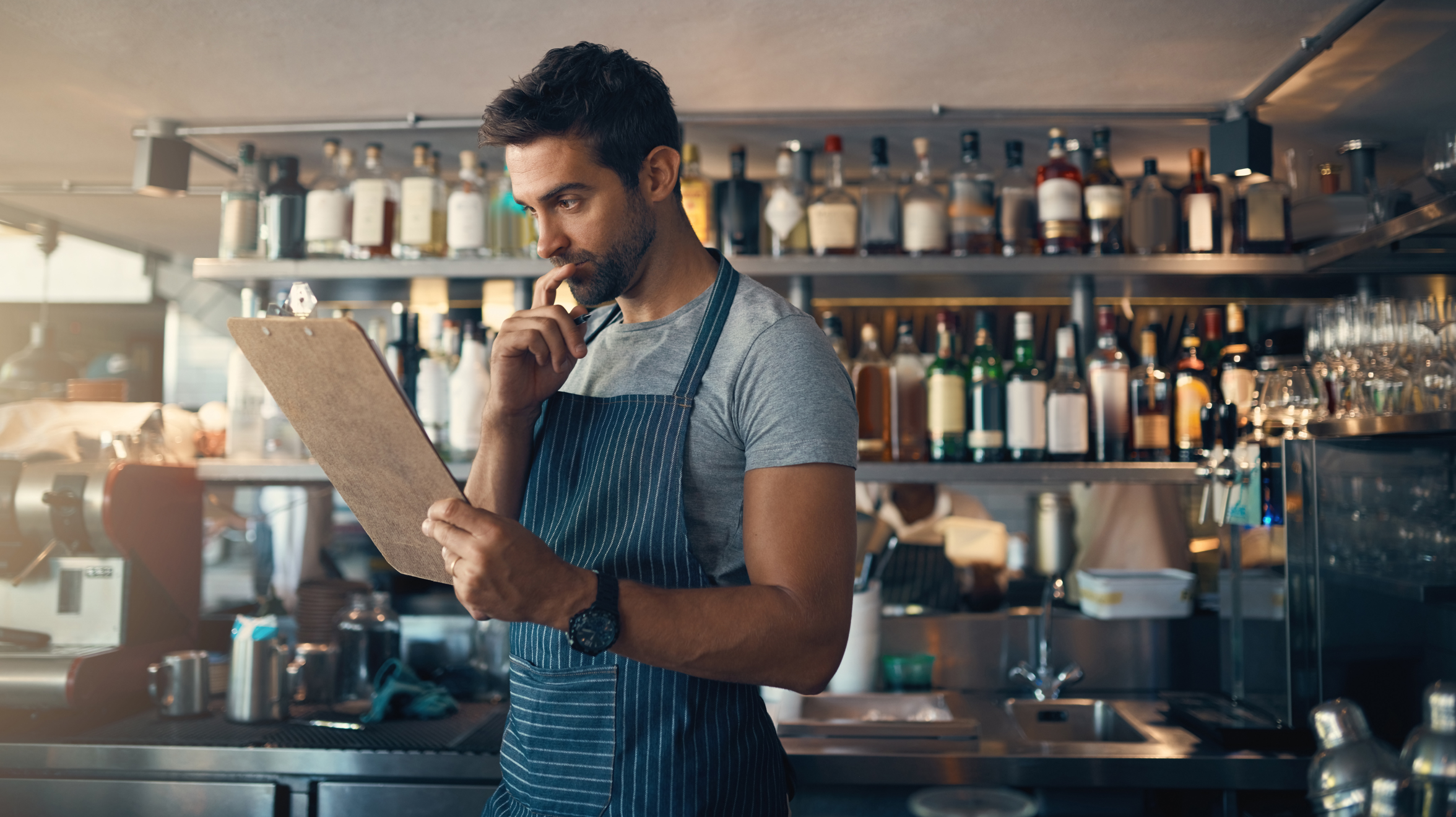 Man in bar wearing an apron, staring at a clipboard